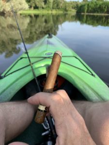 A kayak on the river, a fishing pole and a cigar